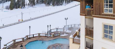 A hotel with a pool area, including a hot tub and a small pool, surrounded by snowy landscape and ski slopes.
