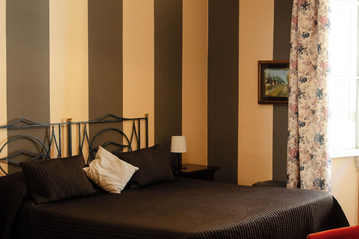Une chambre à coucher avec un lit, une chaise rouge, une lampe et un tableau accroché au mur.