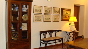 A dining area with a wooden table, bench, and a cabinet with glass doors. There are framed pictures on the wall and a clock above the cabinet. - Soggiorno Michelangelo (Florence)