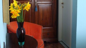 A room with a wooden wardrobe, a vase with flowers, a table, and an orange chair. - Soggiorno Michelangelo (Florence)