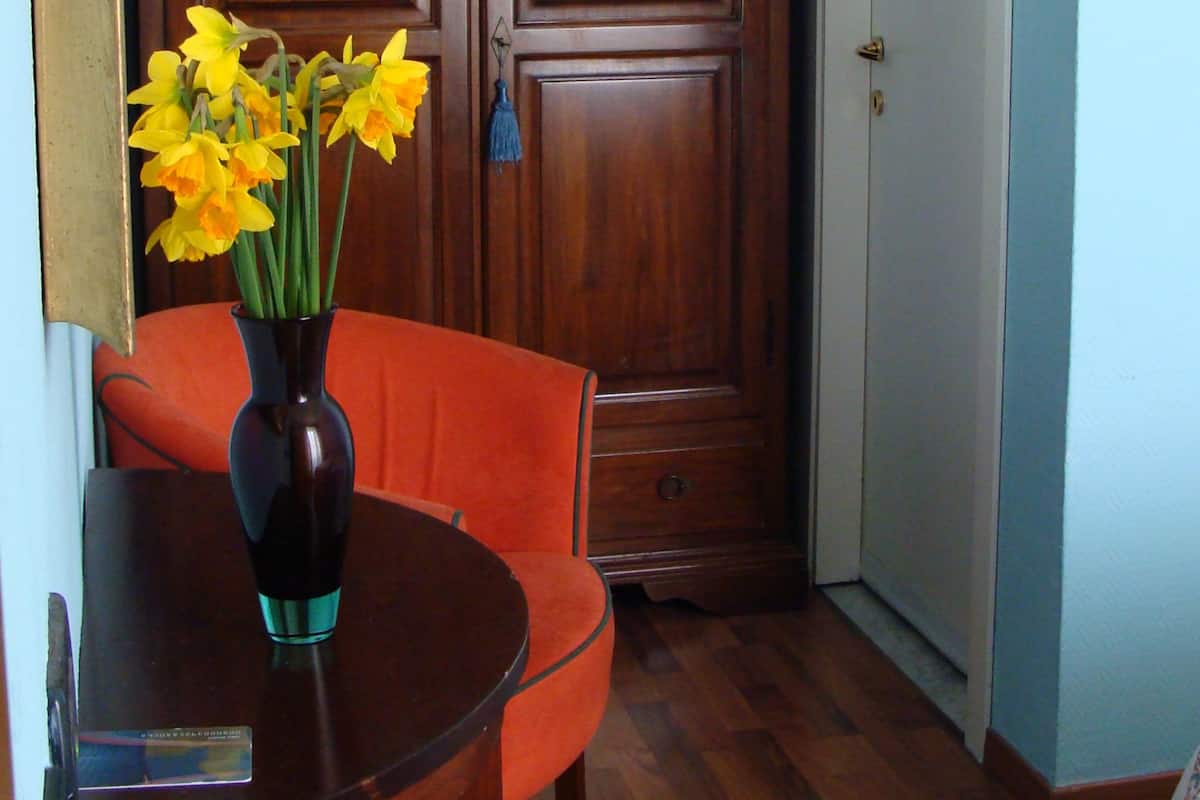 Une pièce avec une armoire en bois, un vase rempli de fleurs, une table et une chaise orange.