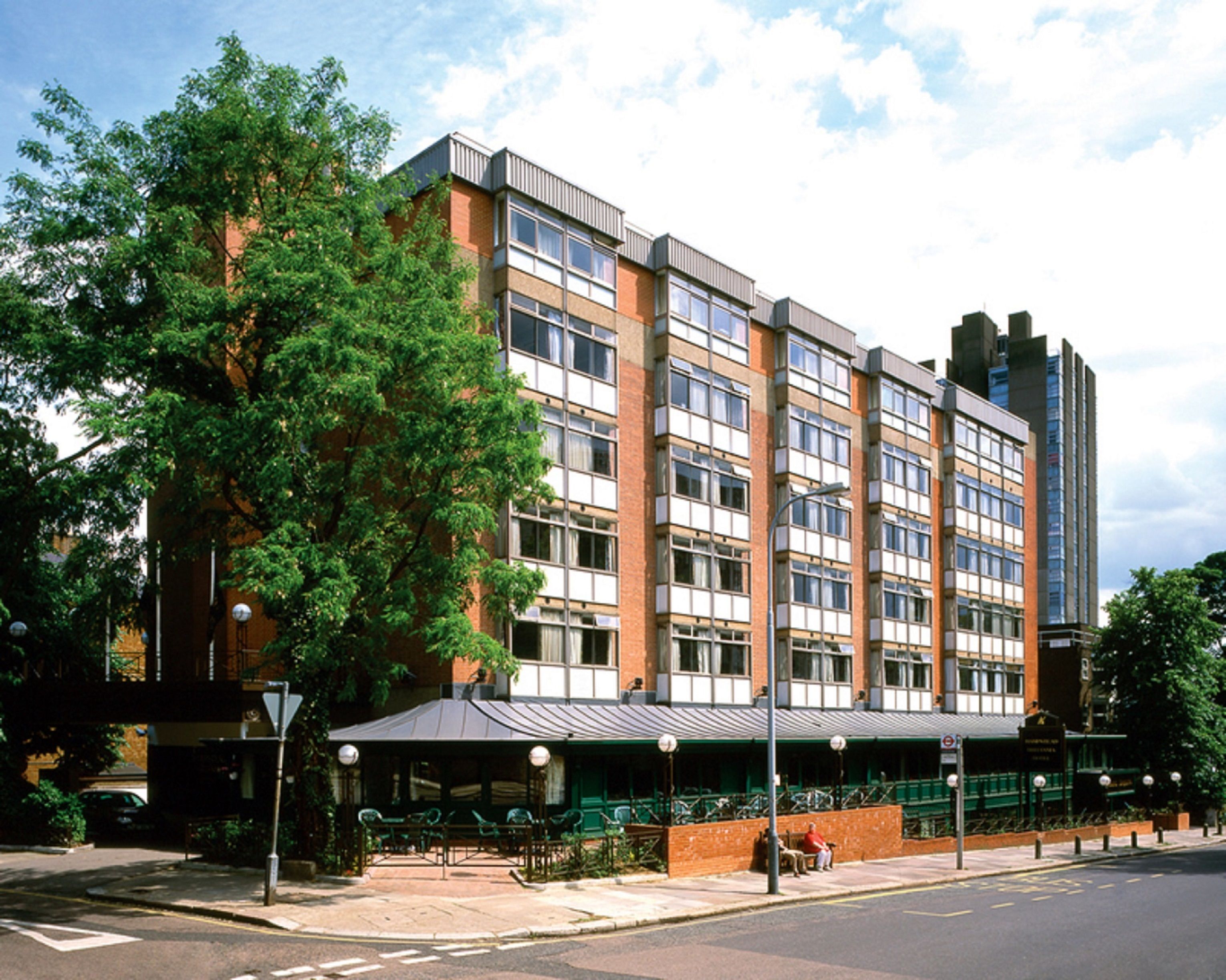 A multi-story hotel with a brick facade, large windows, and a covered outdoor seating area.