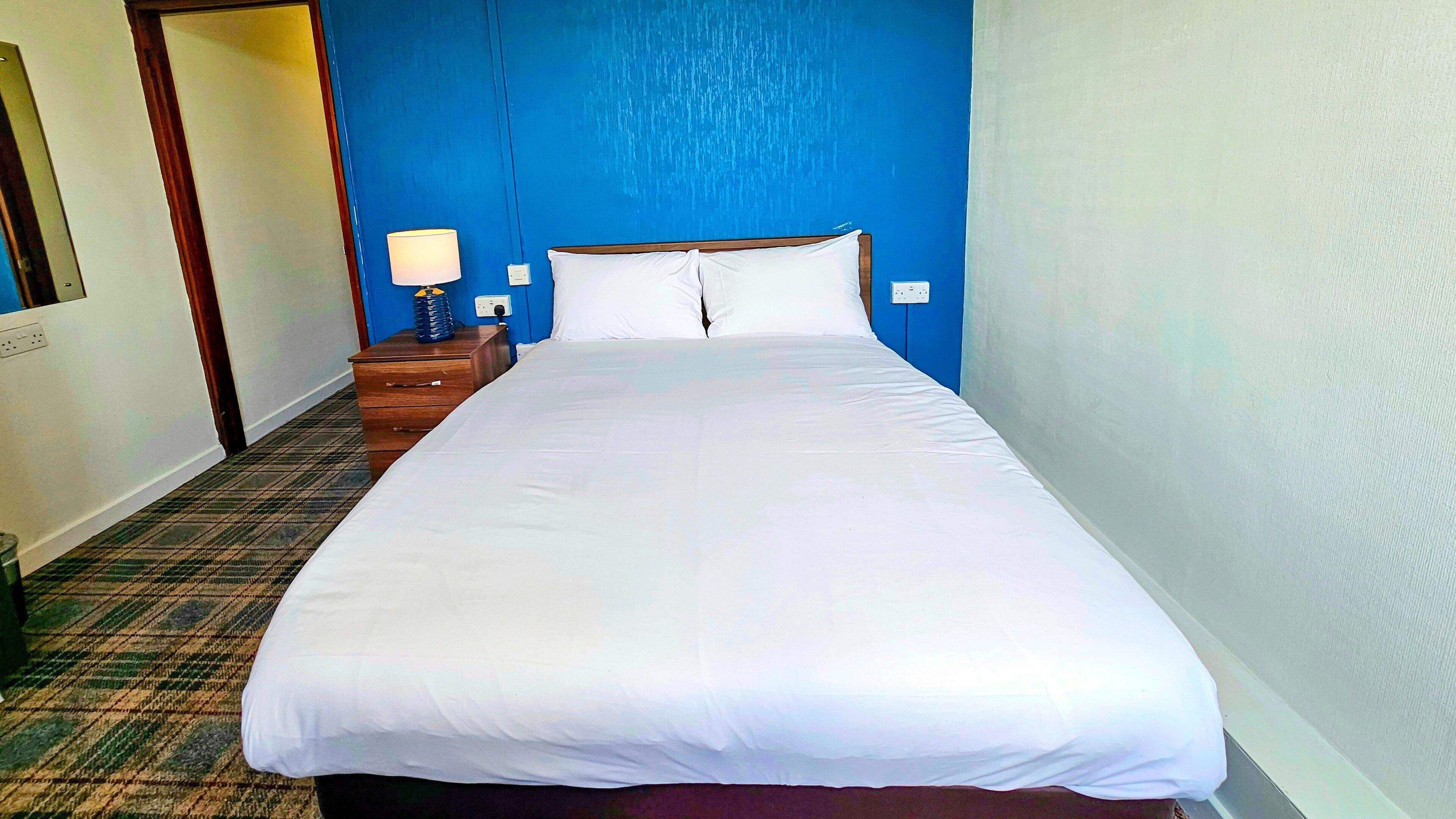 A hotel room with a large bed, a nightstand with a lamp, and a carpeted floor.