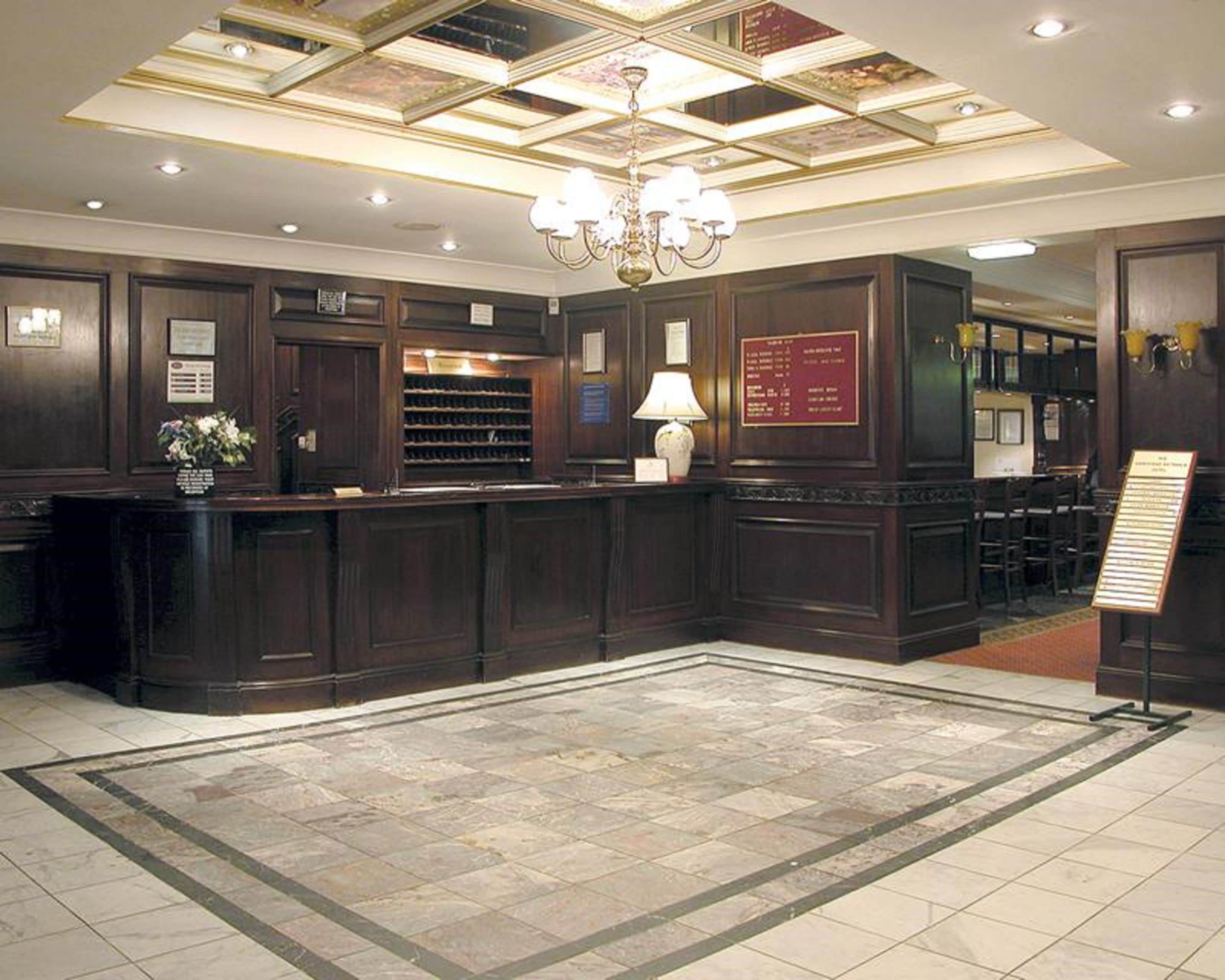 Un'area reception con una scrivania in legno scuro, un lampadario, un espositore per vino e un supporto per il menu.
