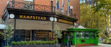 The Hampstead Britannia Hotel with a prominent entrance, a balcony with flags, and a green kiosk.