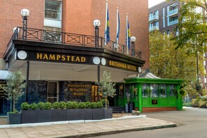 The Hampstead Britannia Hotel with a prominent entrance, a balcony with flags, and a green kiosk.