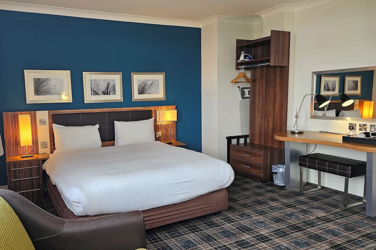 A hotel room with a bed, bedside tables, a desk, a chair, and a wardrobe.