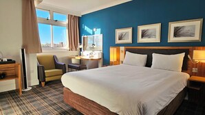 Ein Hotelzimmer mit einem großen Bett, einem Schreibtisch, einem Sessel und einem fenster mit Vorhängen.