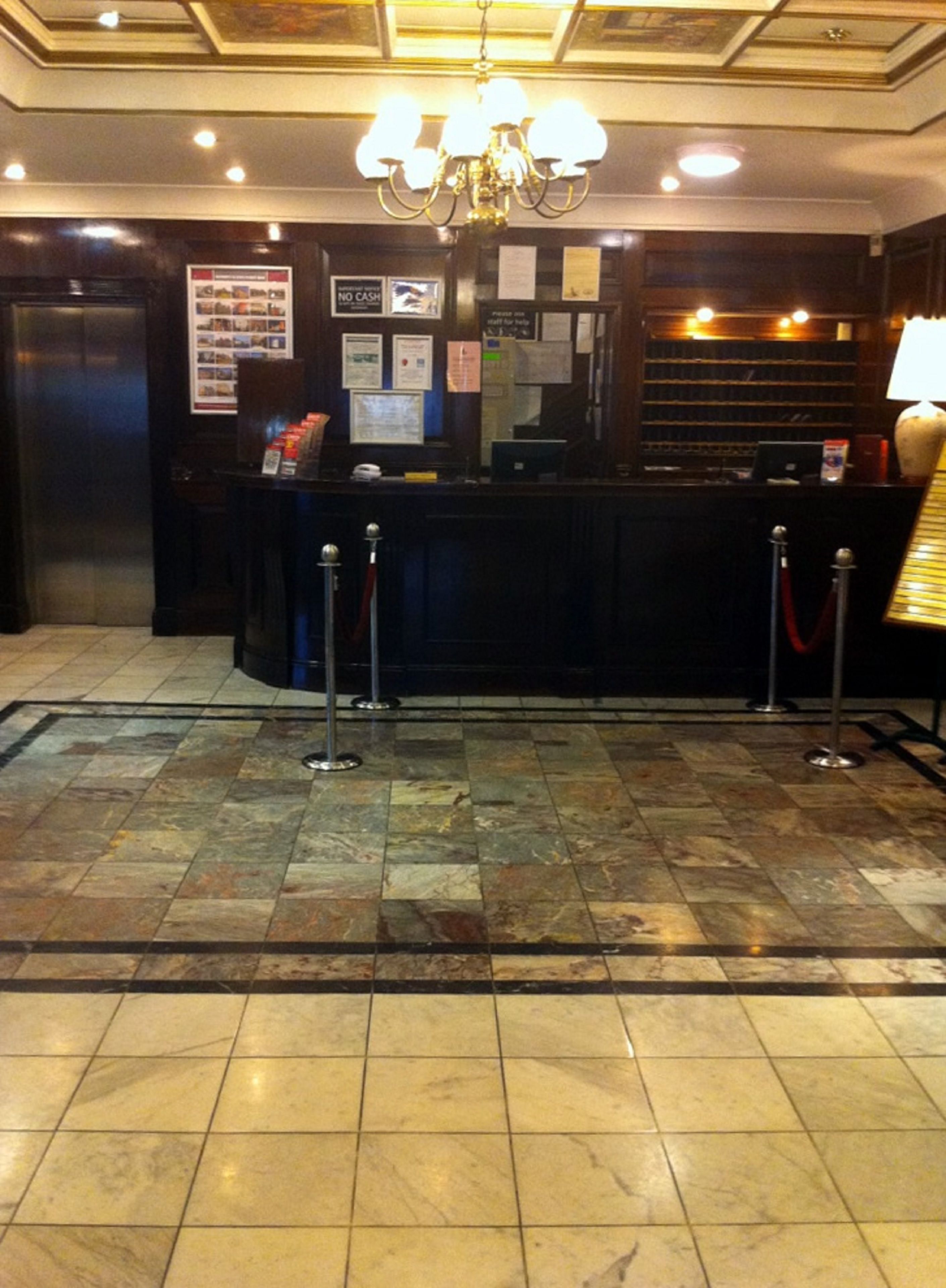 A reception area with a marble floor, a chandelier, a reception desk, and a 'No Cash' sign.