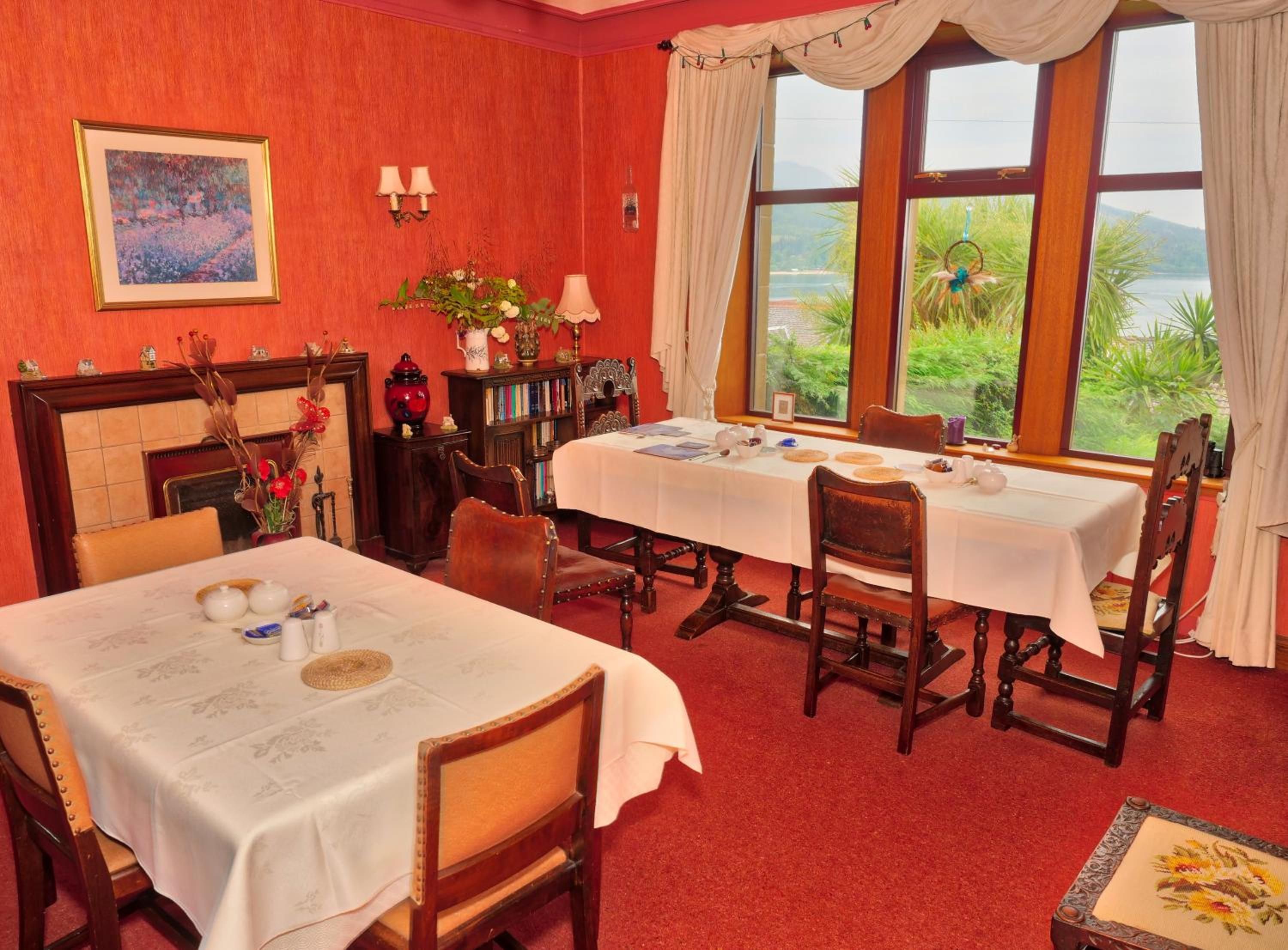 A dining room with a fireplace, a table set for two, and a view of greenery outside.