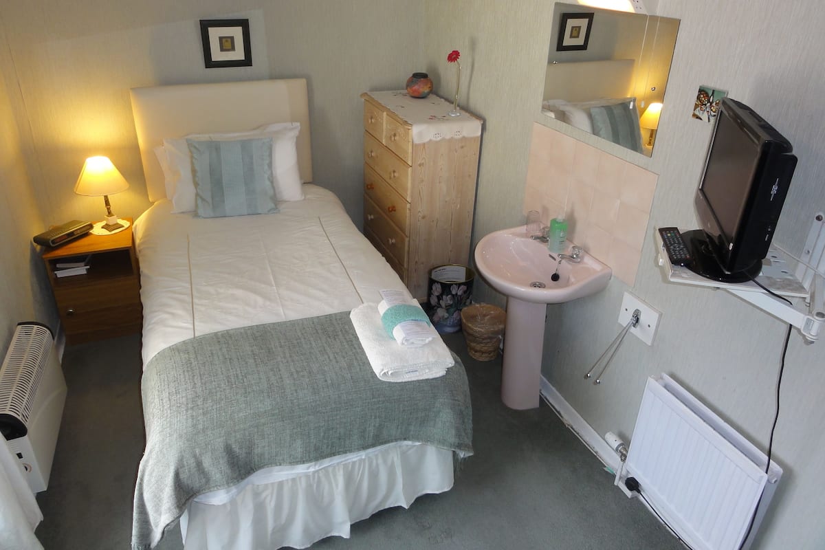A hotel room with a bed, a nightstand with a lamp, a dresser, a sink, and a mirror.