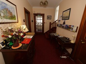 A hallway with a desk, a vase of flowers, a fire exit sign, and a staircase. - Belvedere (Isle of Arran)
