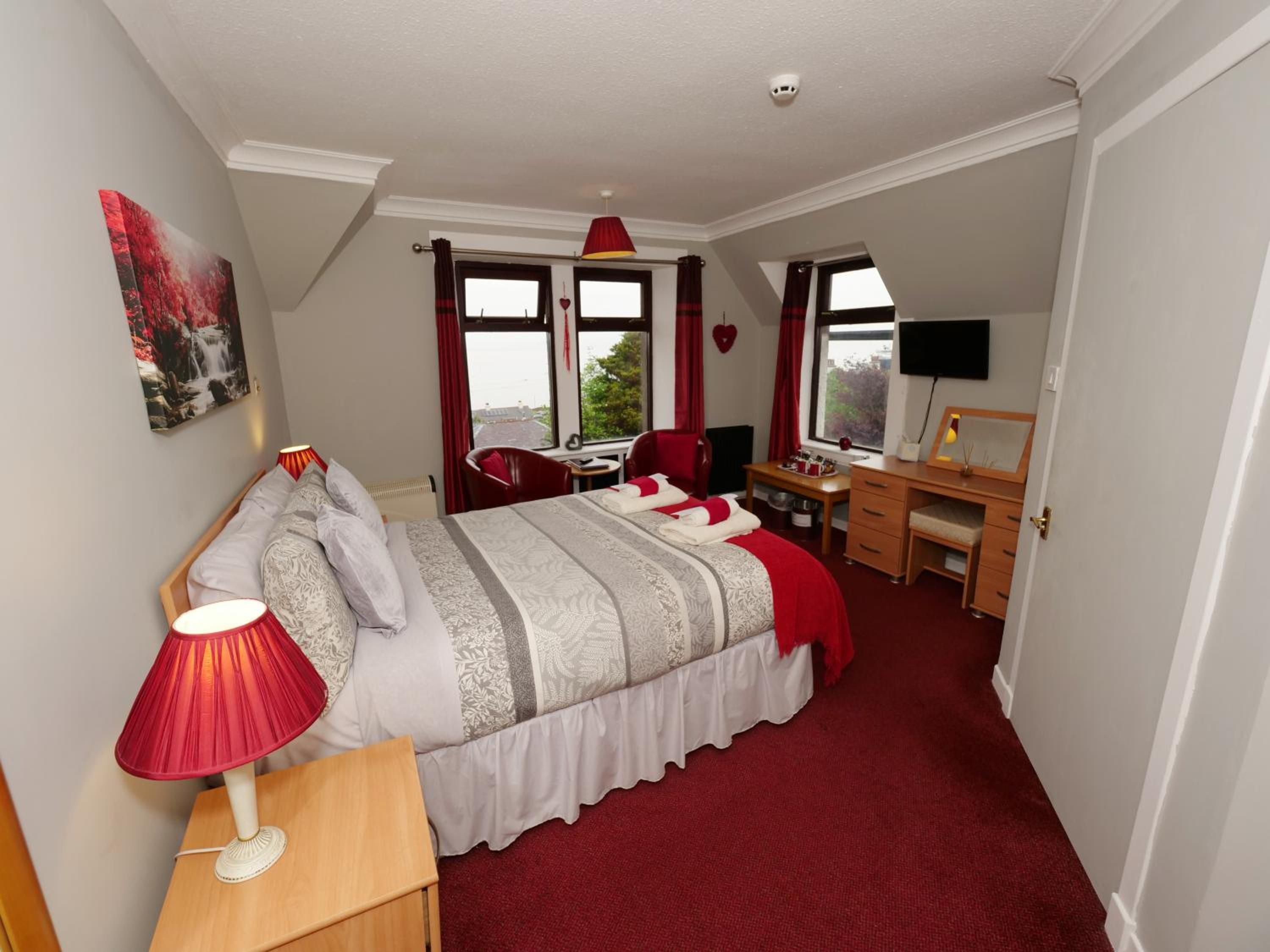 A hotel room with a bed, desk, chair, and a television.