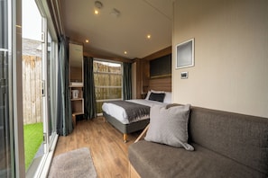 A modern bedroom with a bed, a sofa, a small table, and a window with curtains.