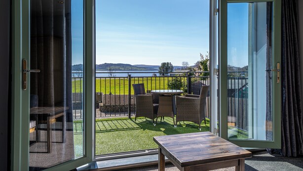 A balcony with a view of a grassy field and a body of water. - The Oak Tree Inn (Balmaha)