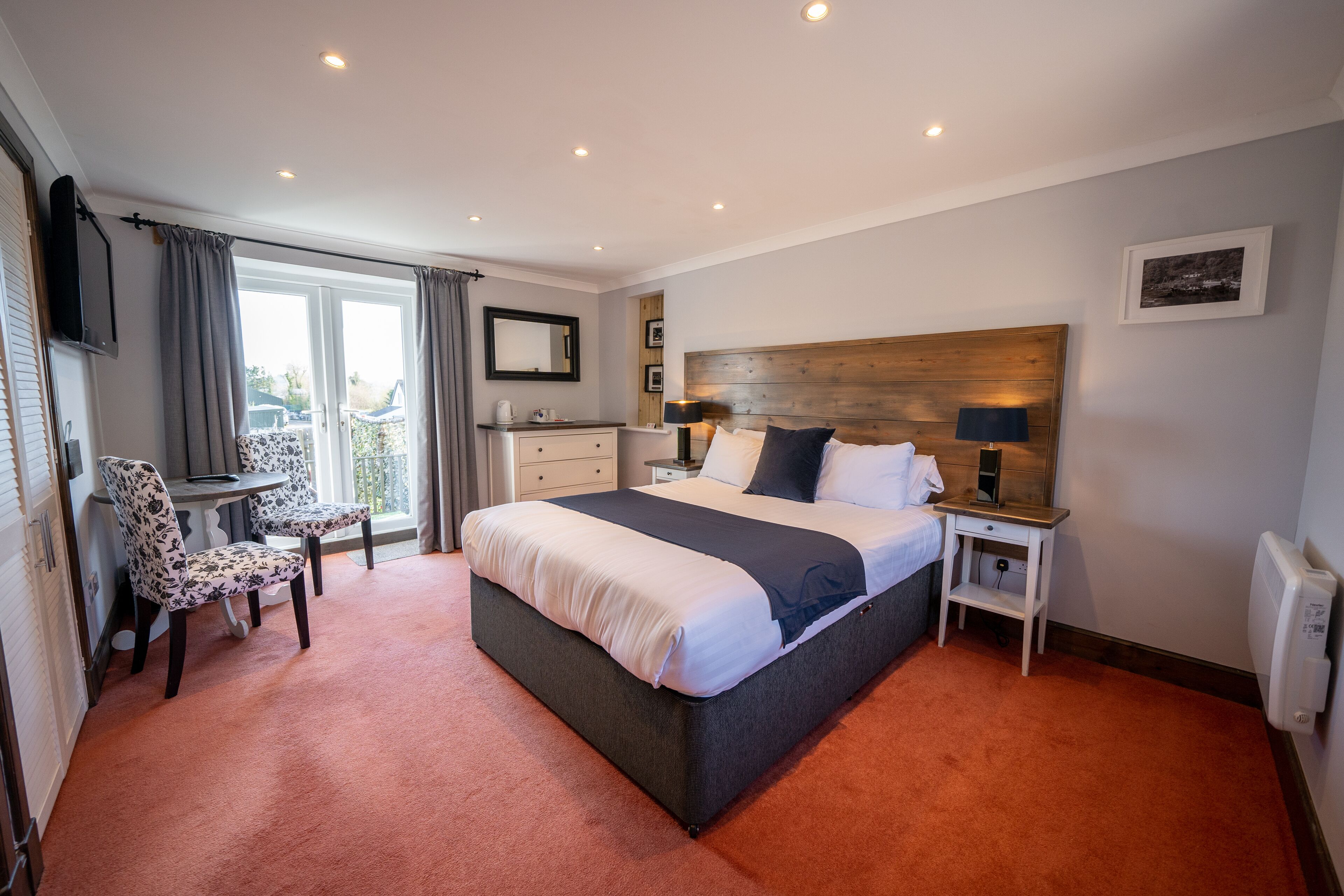 A hotel room with a large bed, a desk with a chair, a small table, a TV, and a window with curtains.