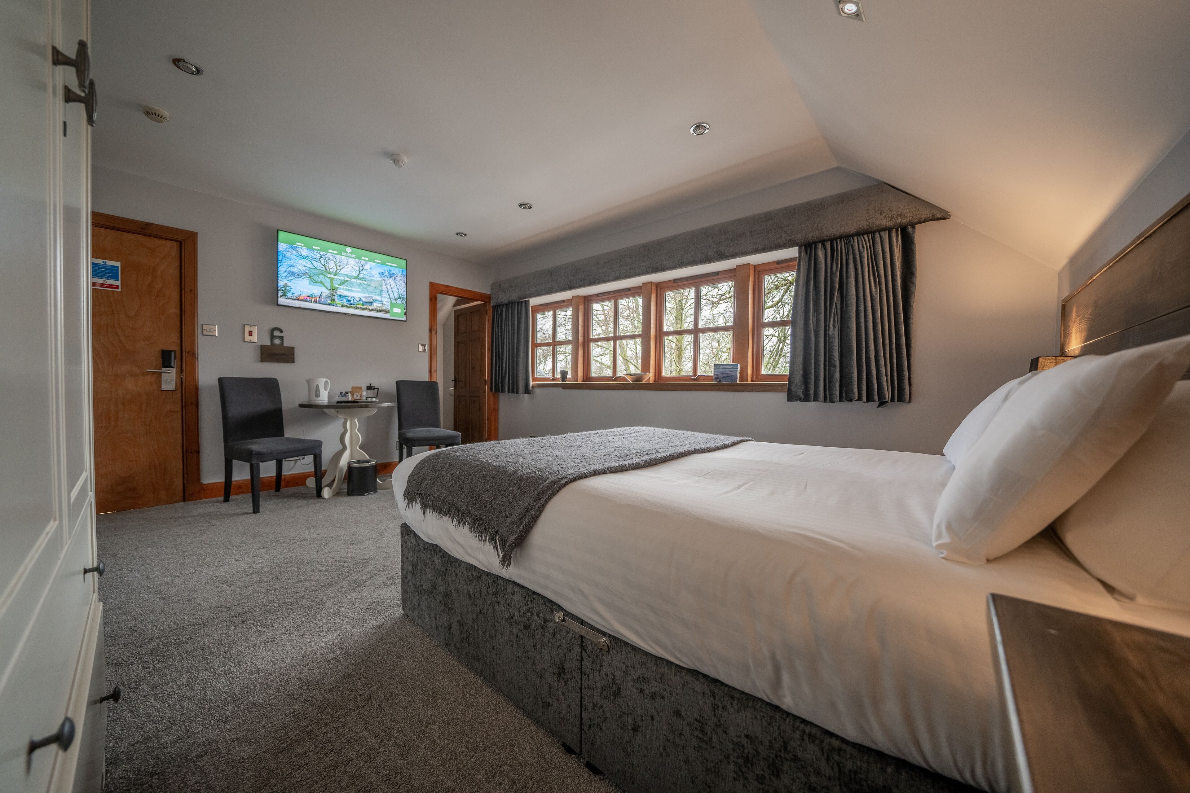 Un dormitorio con una cama grande, un escritorio y un televisor montado en la pared.
