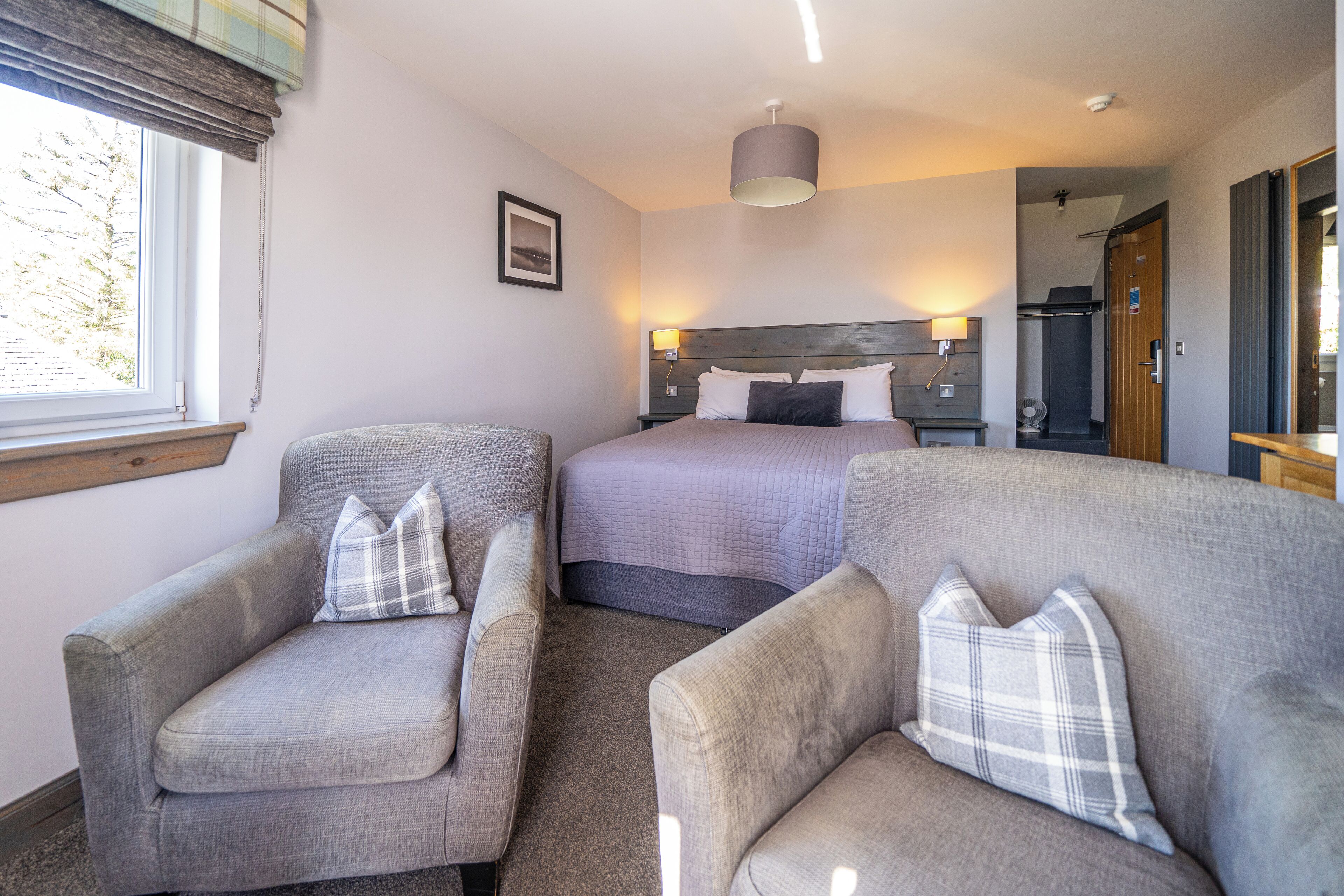 A hotel room with a bed, two armchairs, a bedside table, a lamp, and a window with curtains.