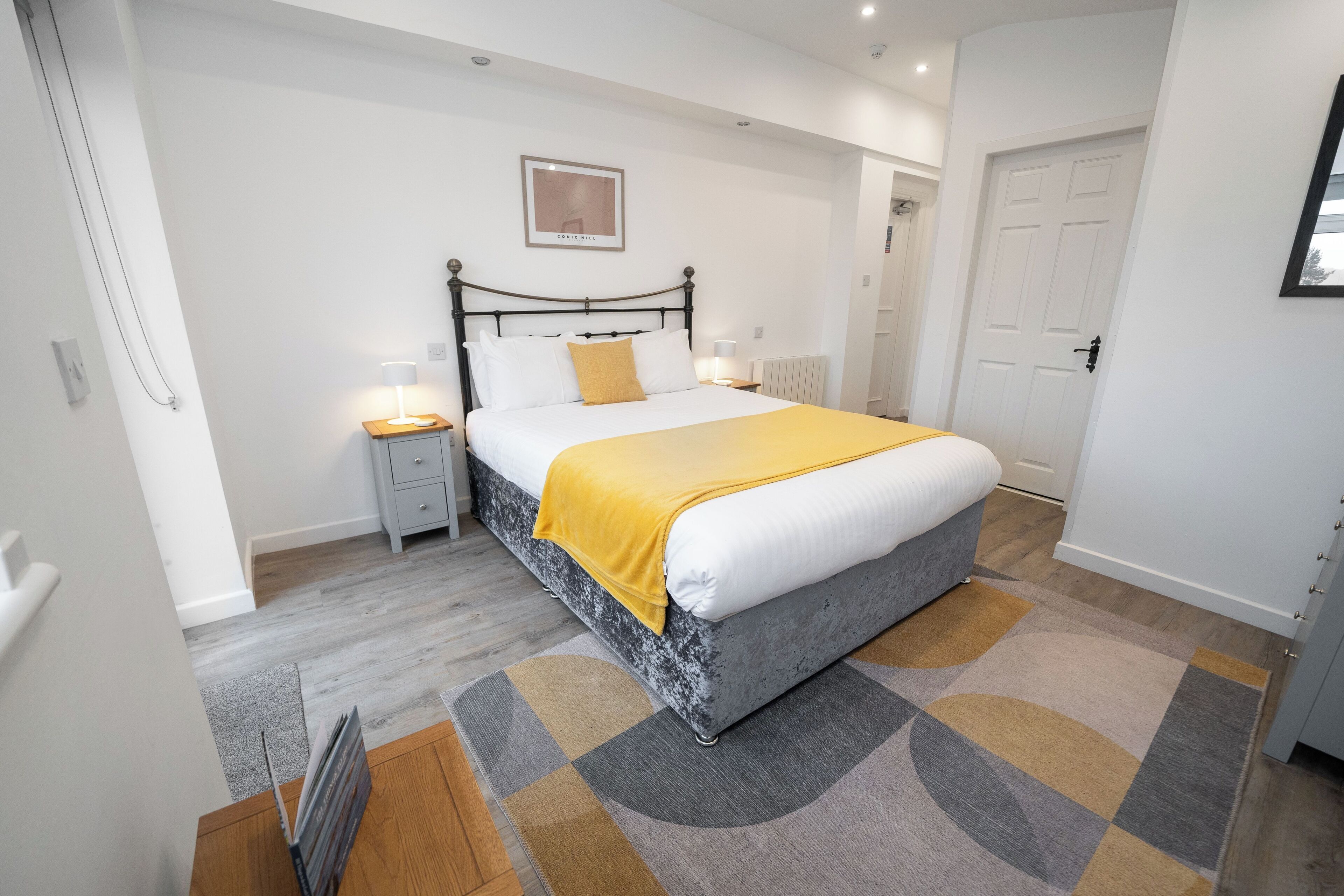 Un dormitorio con cama, mesitas de noche, radiador y una puerta.