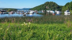 A marina with boats docked, surrounded by lush greenery and hills in the background. - The Oak Tree Inn (Balmaha)