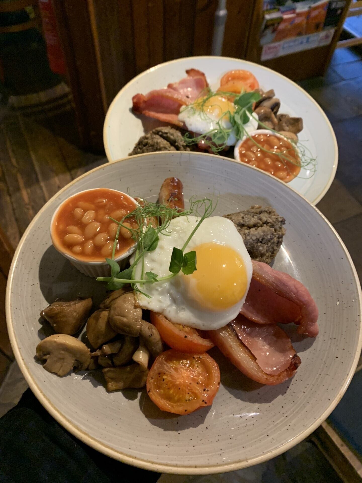 Two plates of breakfast with eggs, bacon, mushrooms, tomatoes, and beans.