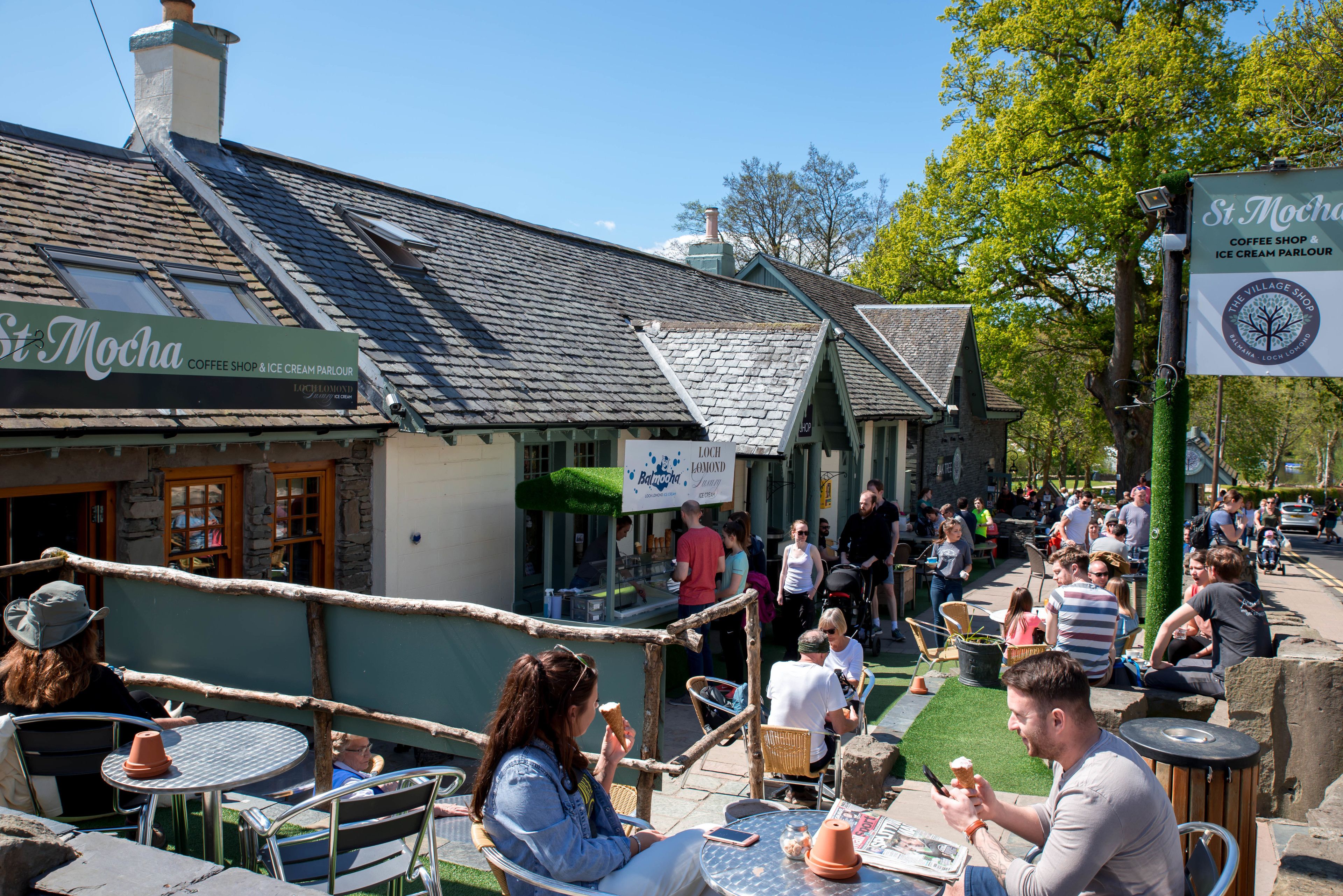 An outdoor seating area with tables and chairs, a sign for 'St. Mocha Coffee Shop & Ice Cream Parlour', and a crowd of people.