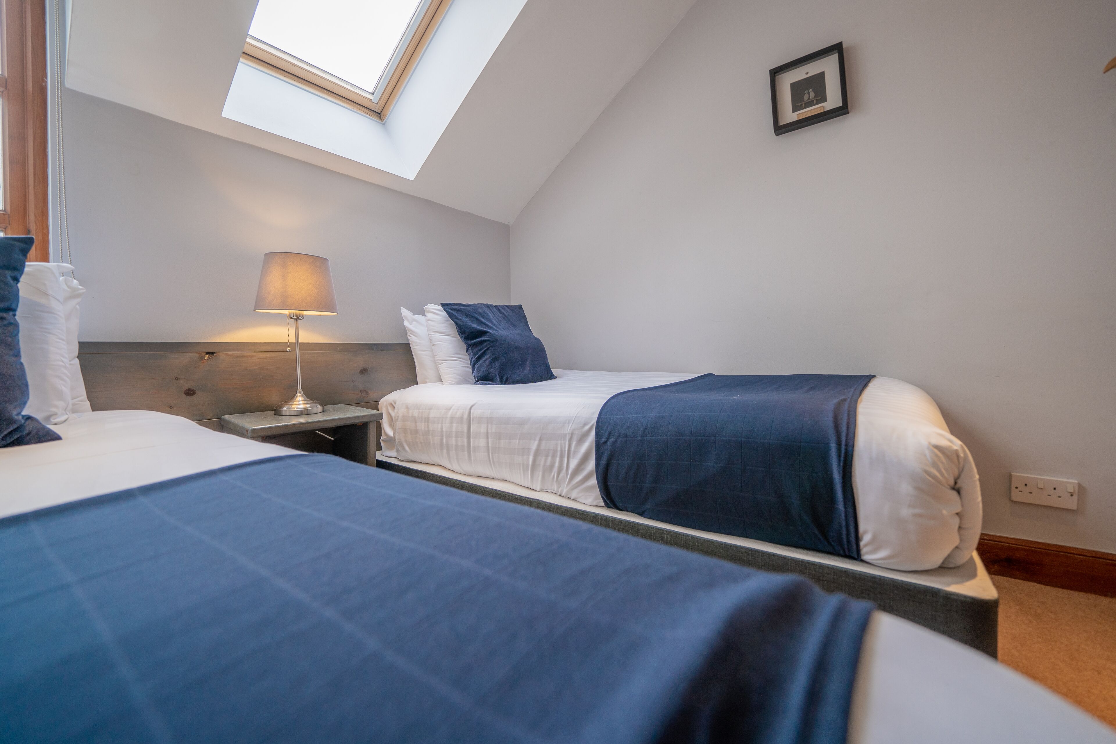 Ein Hotelzimmer mit zwei Betten, einem Oberlicht, einem Nachttisch mit Lampe und einem gerahmten Bild an der Wand.