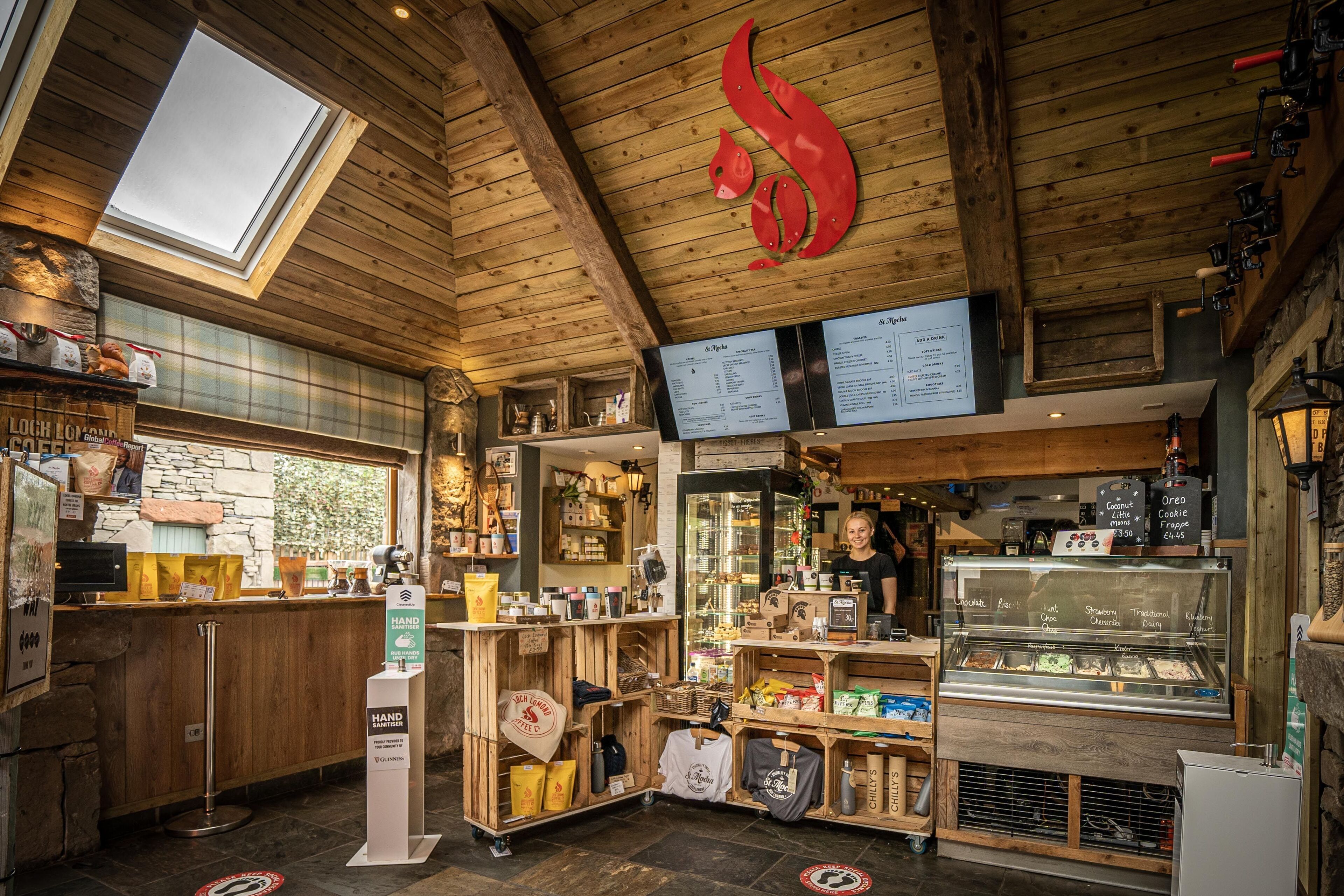 Een gezellig café met houten inrichting, een glazen vitrine met desserts en een menubord boven de toonbank.