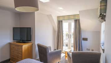 Habitación de hotel con cama, televisor sobre una cómoda de madera, dos sillones, una mesita y una ventana con cortinas.