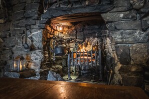 A stone fireplace with a fire, a lantern, and a kettle.