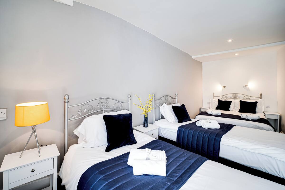 A hotel room with two beds, a nightstand with a lamp, and a vase with flowers.