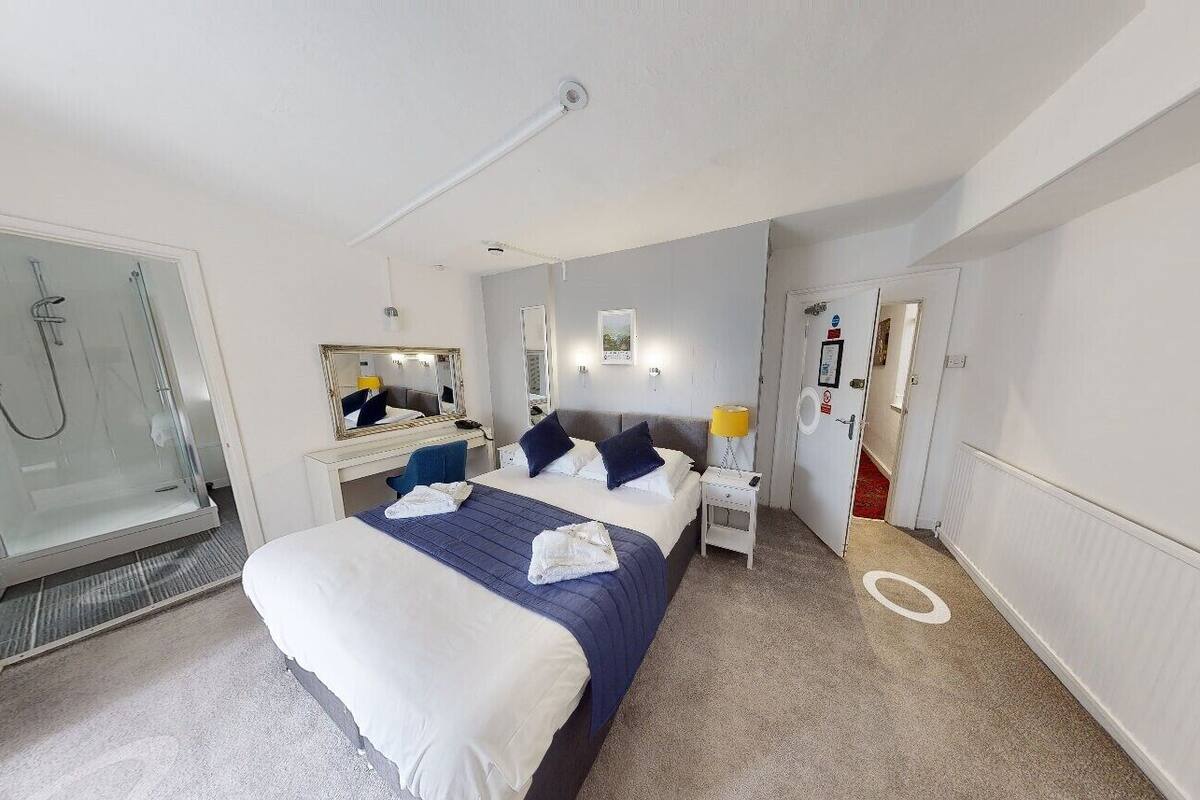 A hotel room with a bed, bedside table, mirror, and a shower area.