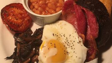 Une assiette composée d’un œuf au plat, de lardons, de saucisses, de pain grillé, de haricots et d’une tomate grillée.