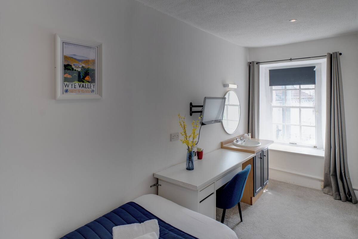 A hotel room with a bed, desk, chair, and a window with curtains.