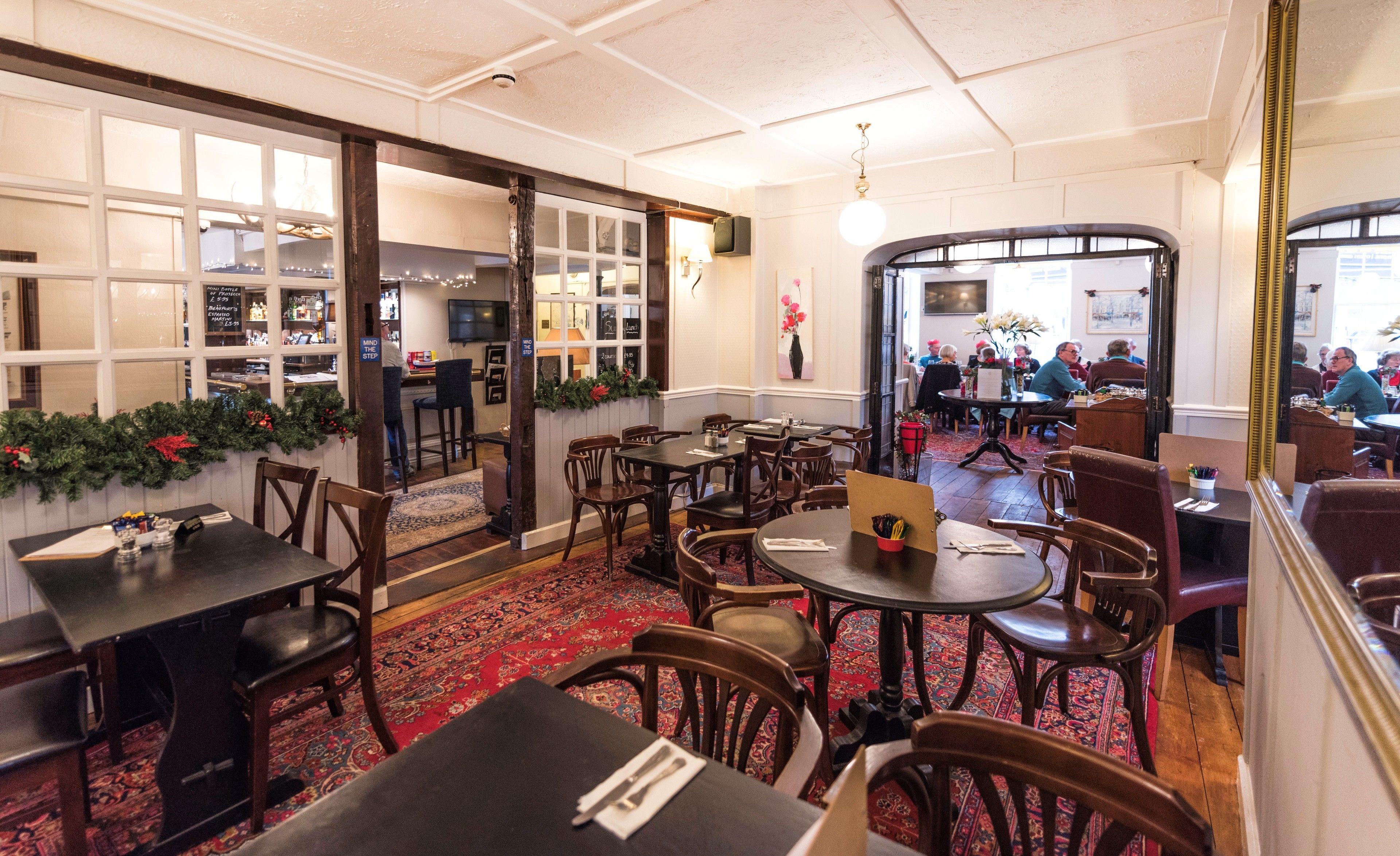 Un restaurante con mesas y sillas de madera, alfombra roja y decoración navideña.