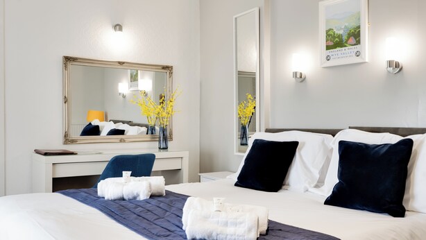 A hotel room with a large bed, a desk, a mirror, and a framed picture on the wall. - The Beaufort Hotel (Chepstow)
