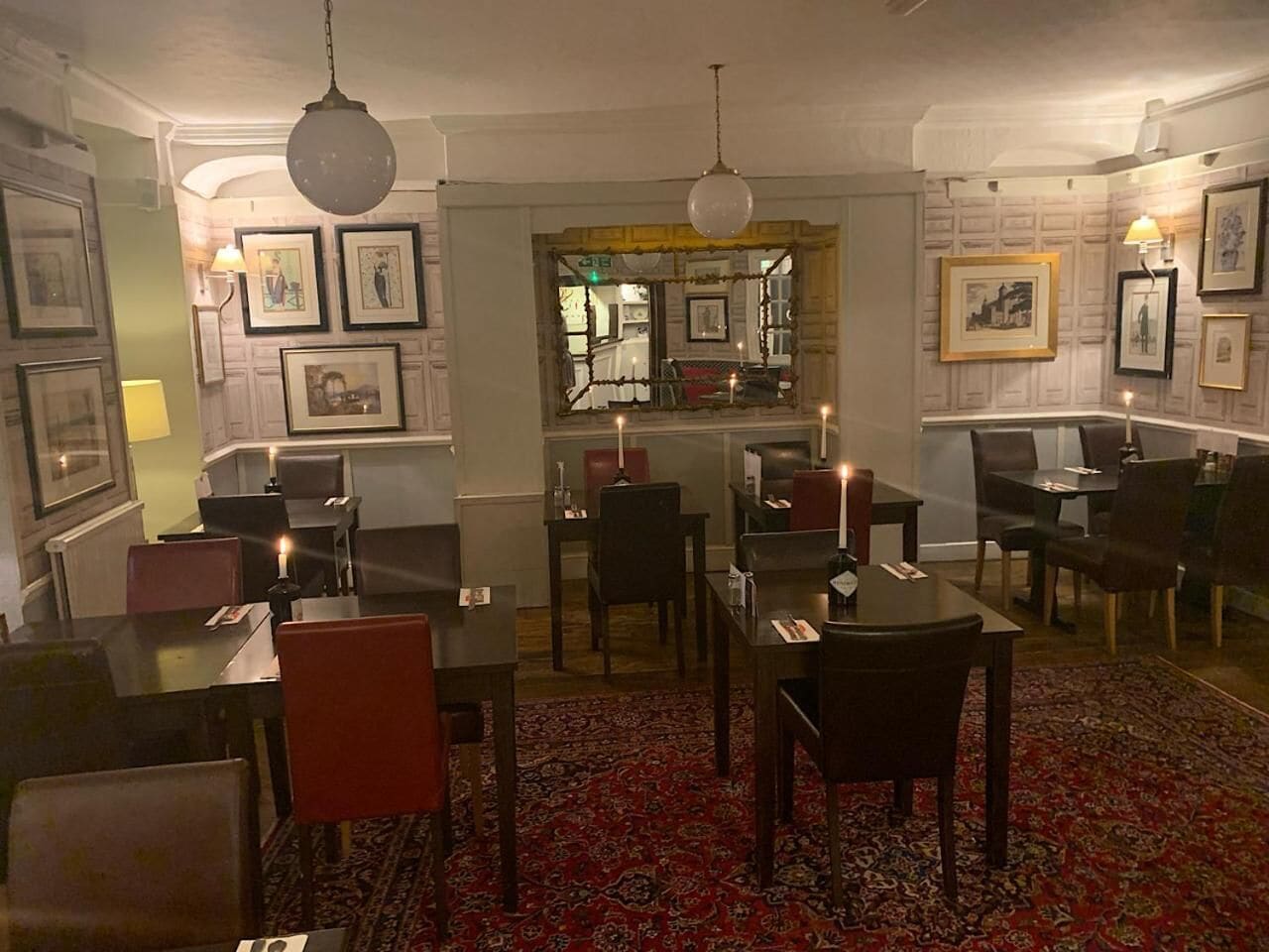 A dining area with tables and chairs, framed pictures on the walls, and a patterned carpet.
