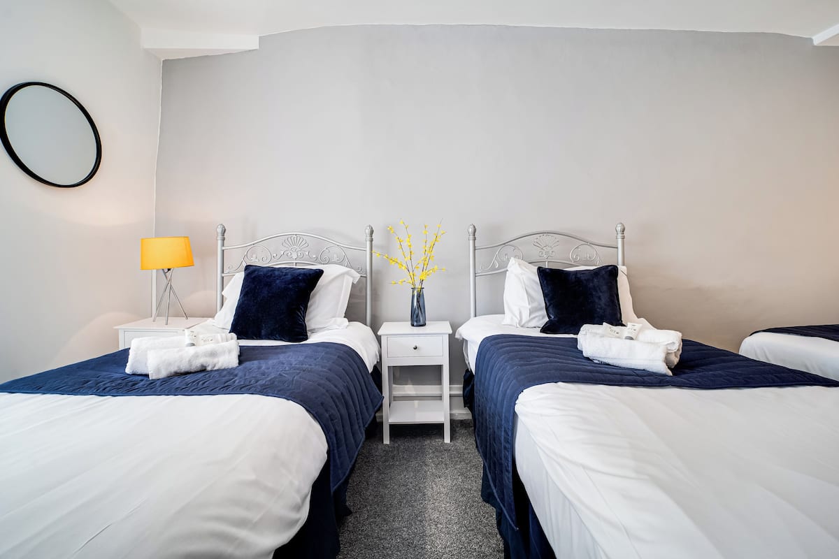 A hotel room with two beds, a nightstand with a lamp, and a vase with flowers.