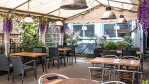 An outdoor patio area with tables and chairs, covered by a canopy, and surrounded by greenery. - The Beaufort Hotel (Chepstow)
