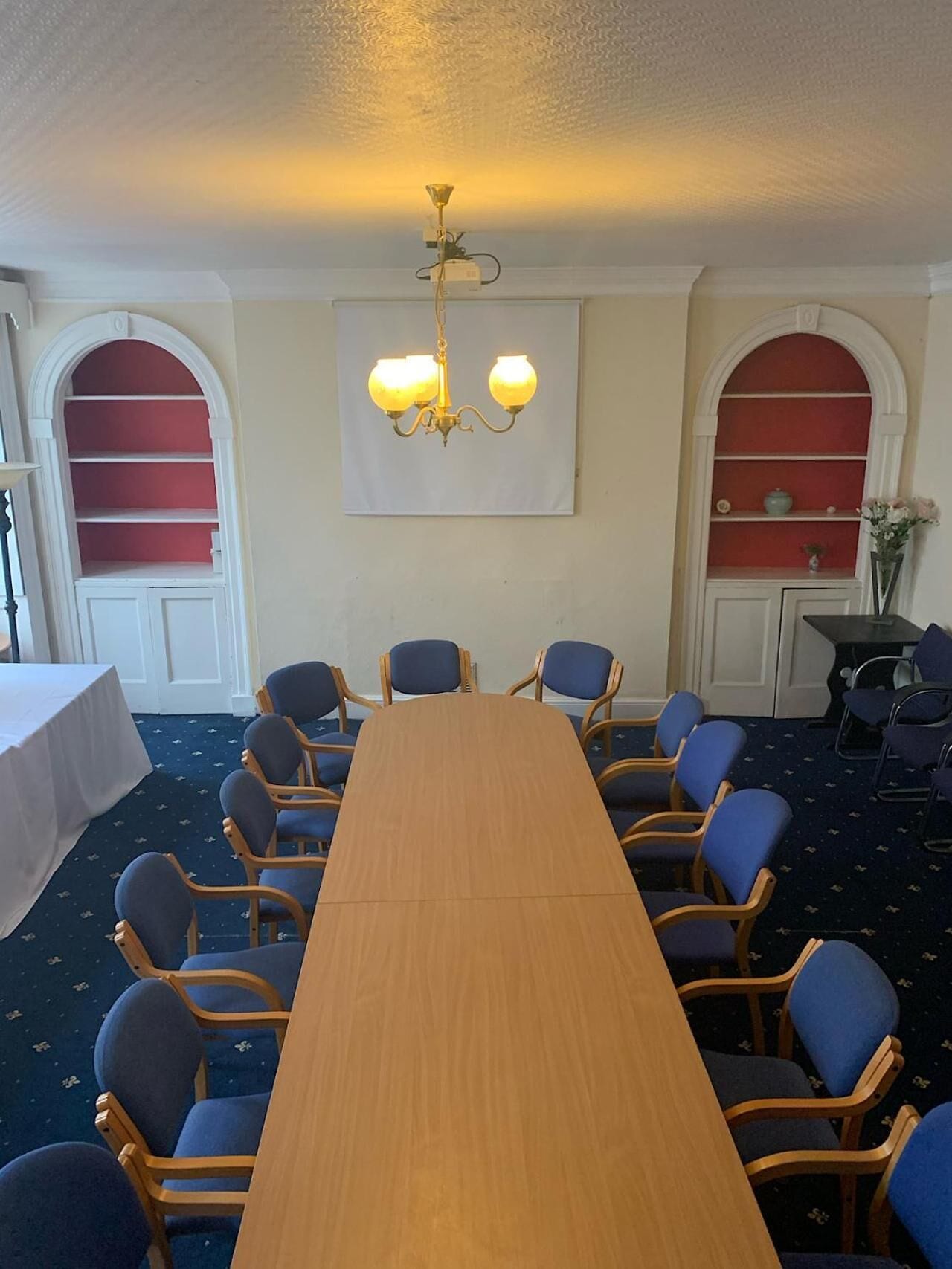 A conference room with a long wooden table, blue upholstered chairs, a chandelier, and red shelving units.