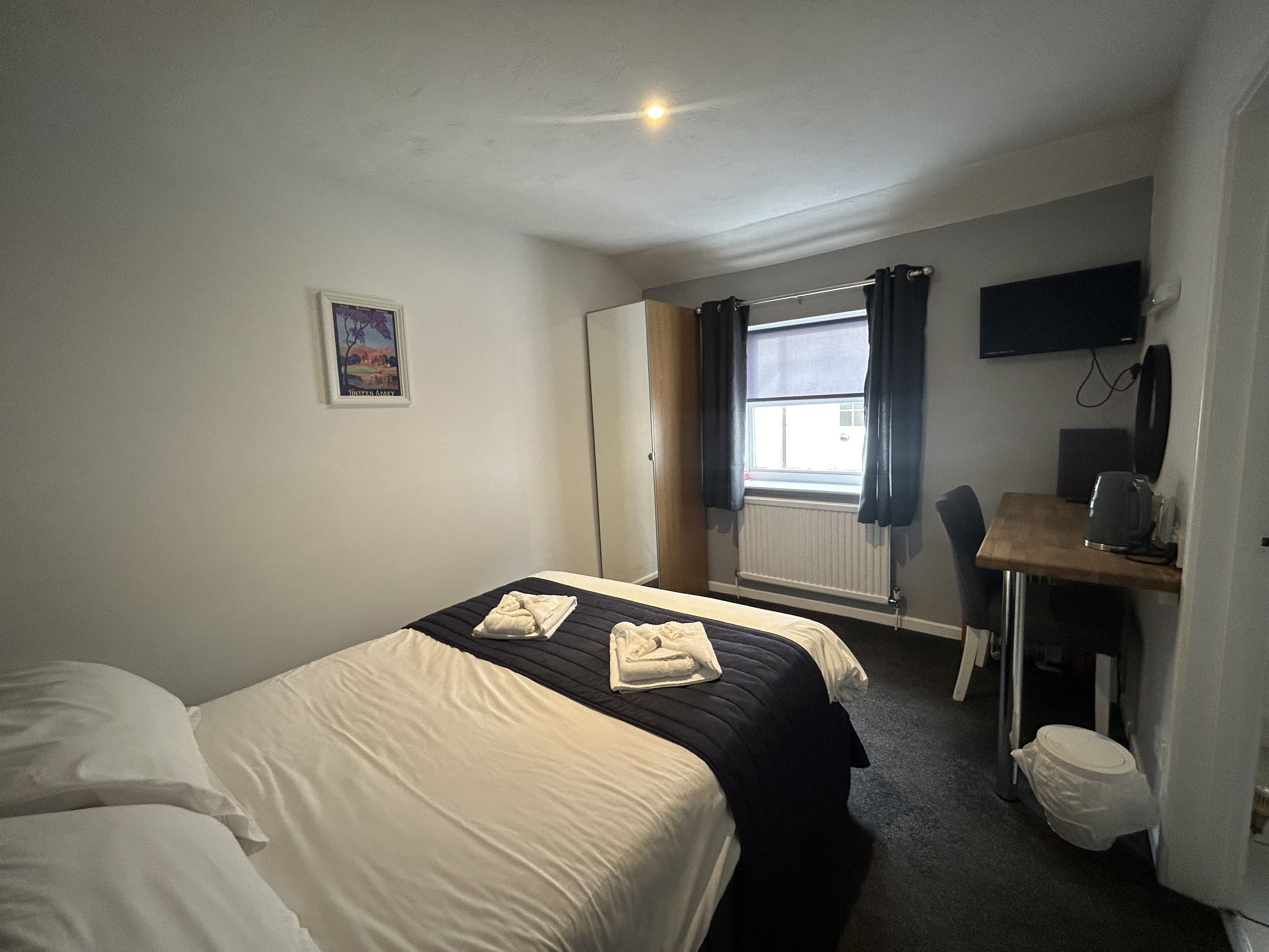 A hotel room with a bed, a desk, a chair, a television, and a window with curtains.