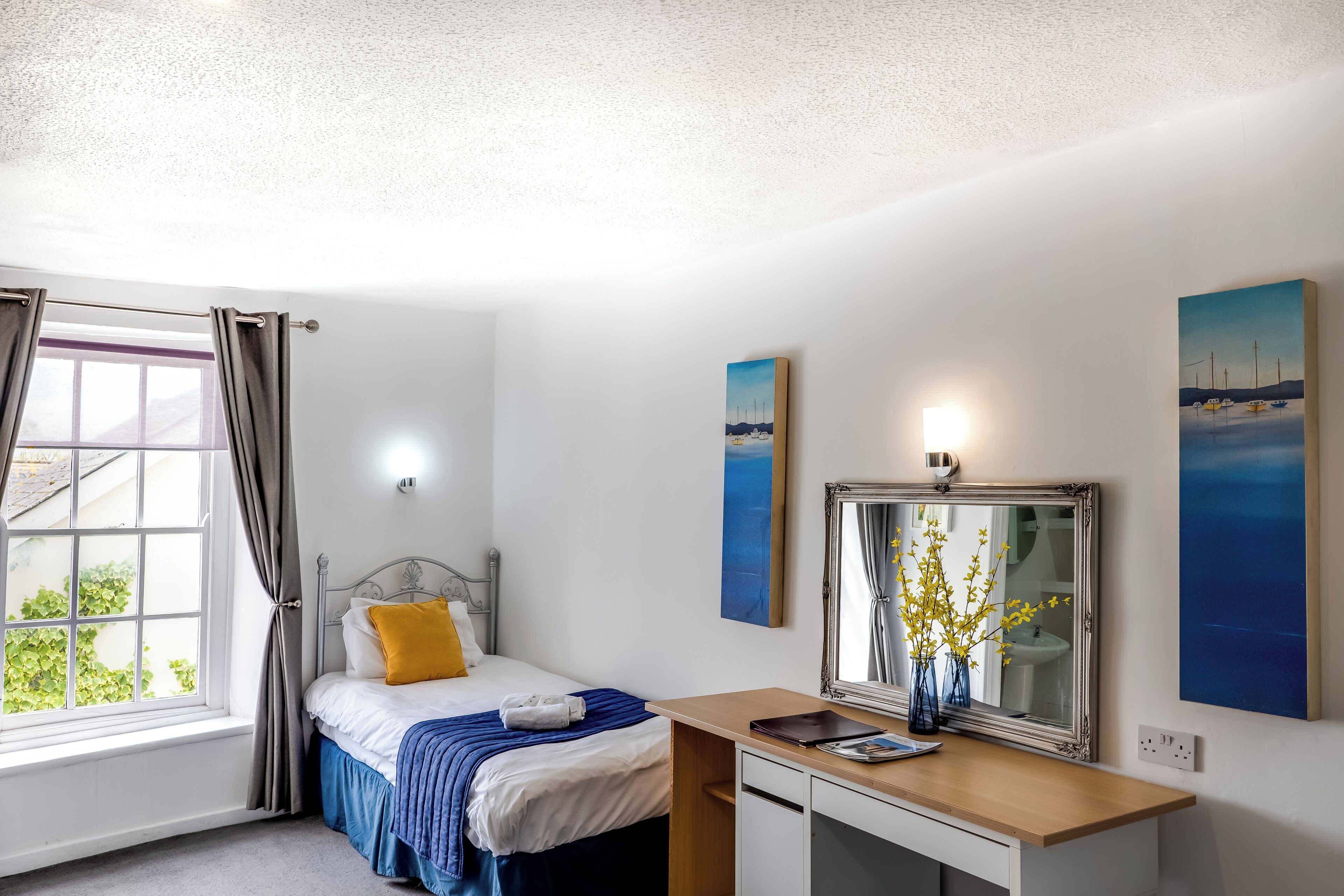 A bedroom with a bed, a desk, a mirror, and artwork on the walls.