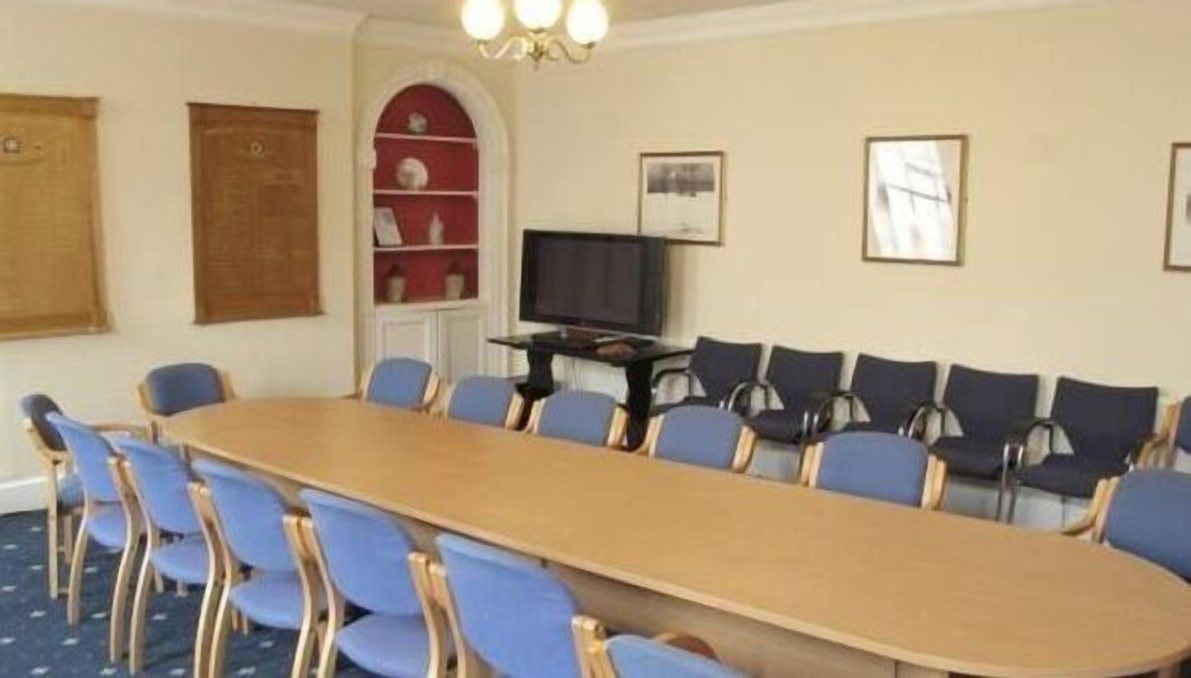 A conference room with a long table and blue chairs, a television, and framed pictures on the wall.