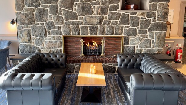 A stone fireplace with a fire, two leather sofas, and a coffee table in a room with a stone wall. - The Cabarfeidh Hotel (Stornoway)