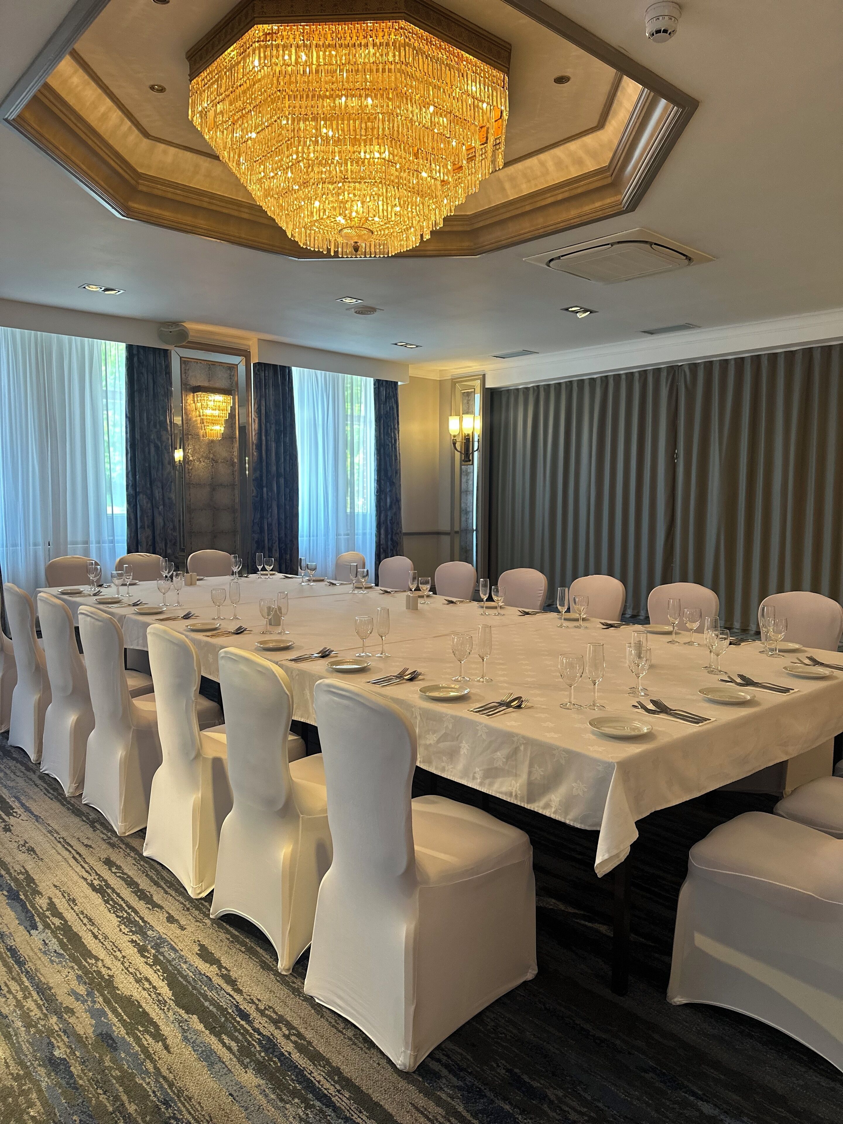 A banquet hall with a large chandelier, white tablecloths, and chairs.