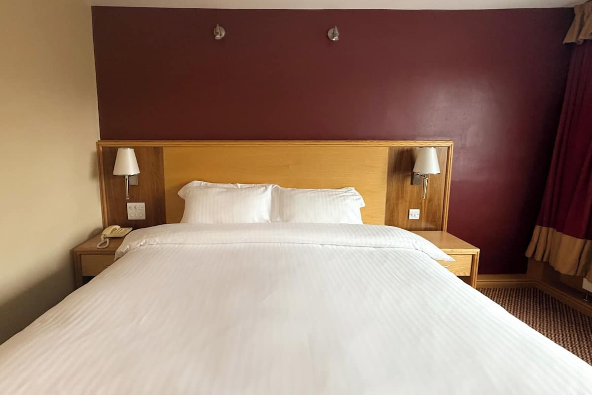 A hotel room with a large bed, two bedside lamps, a telephone, and a wall-mounted light fixture.