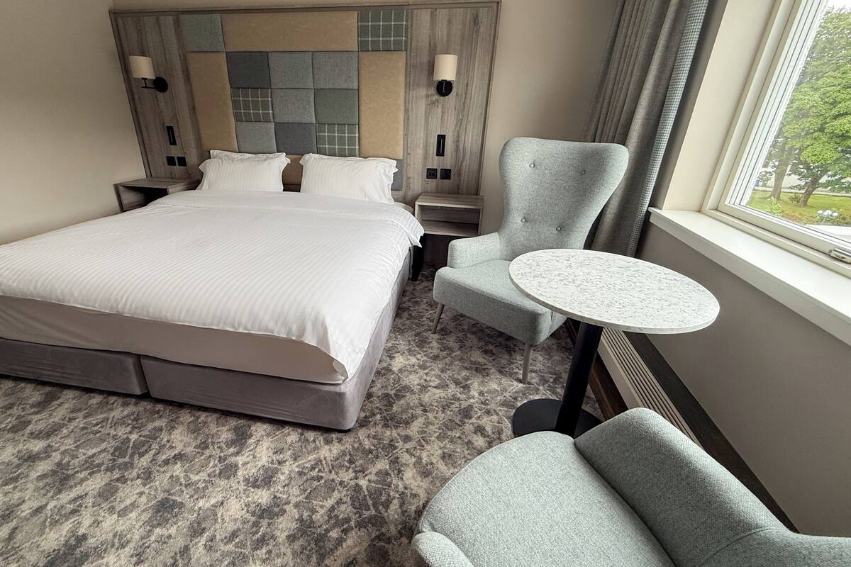 A hotel room with a large bed, two bedside tables, a round table, and a chair.