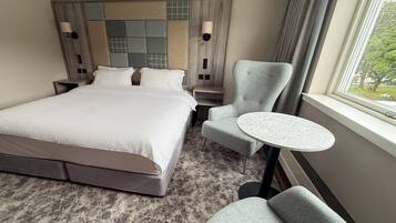 A hotel room with a large bed, two bedside tables, a round table, and a chair.