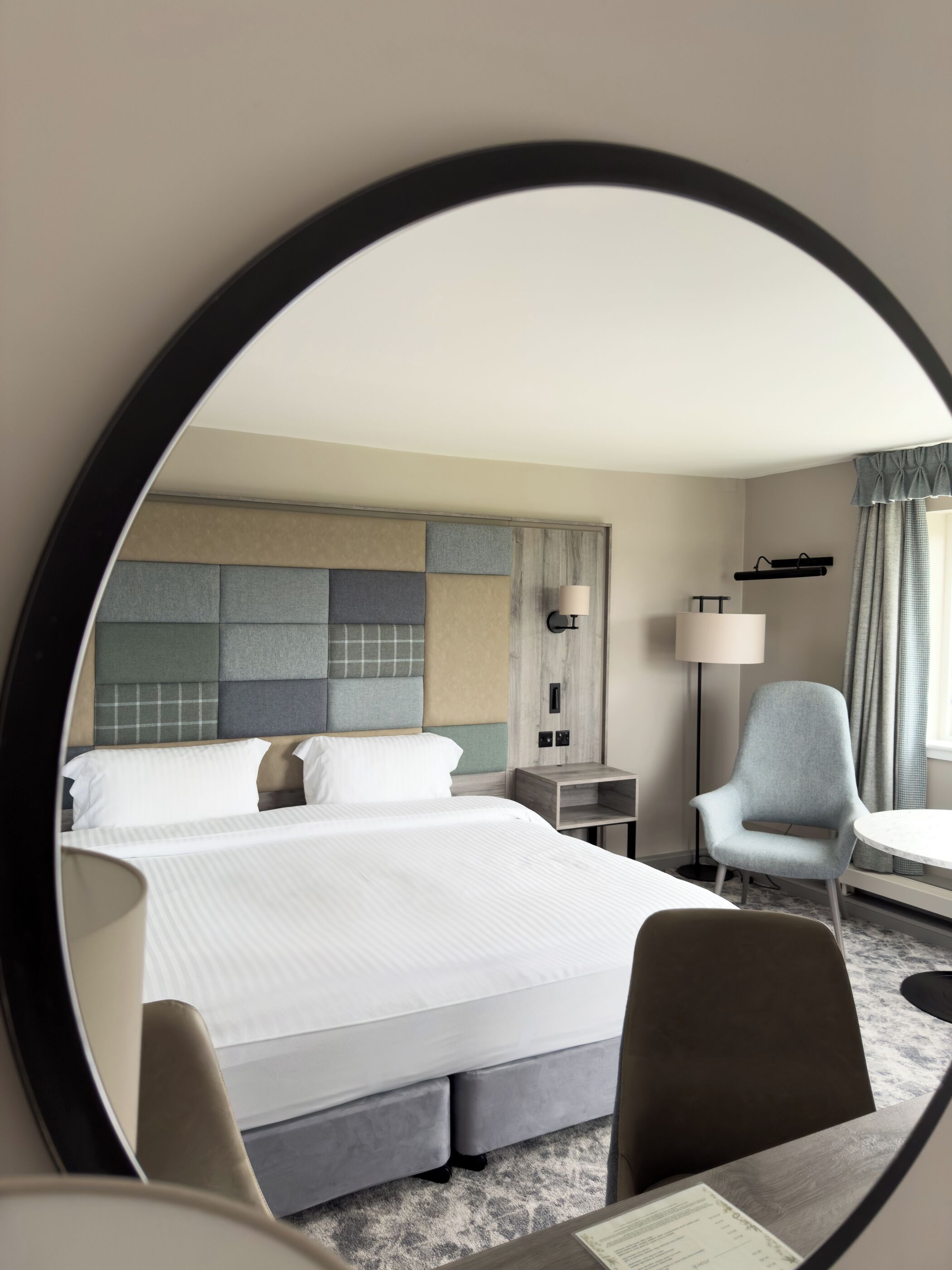 A hotel room with a large bed, a desk, a chair, a lamp, and a mirror.