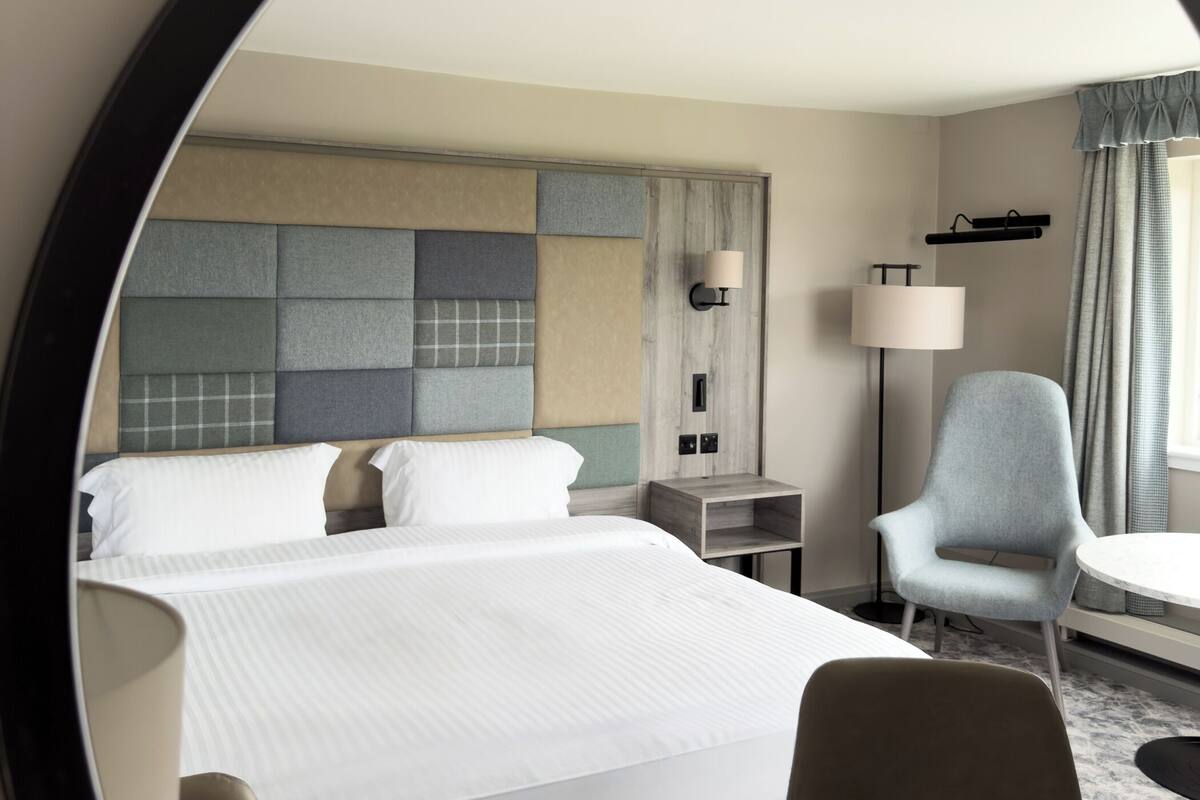 A hotel room with a large bed, a desk, a chair, a lamp, and a mirror.